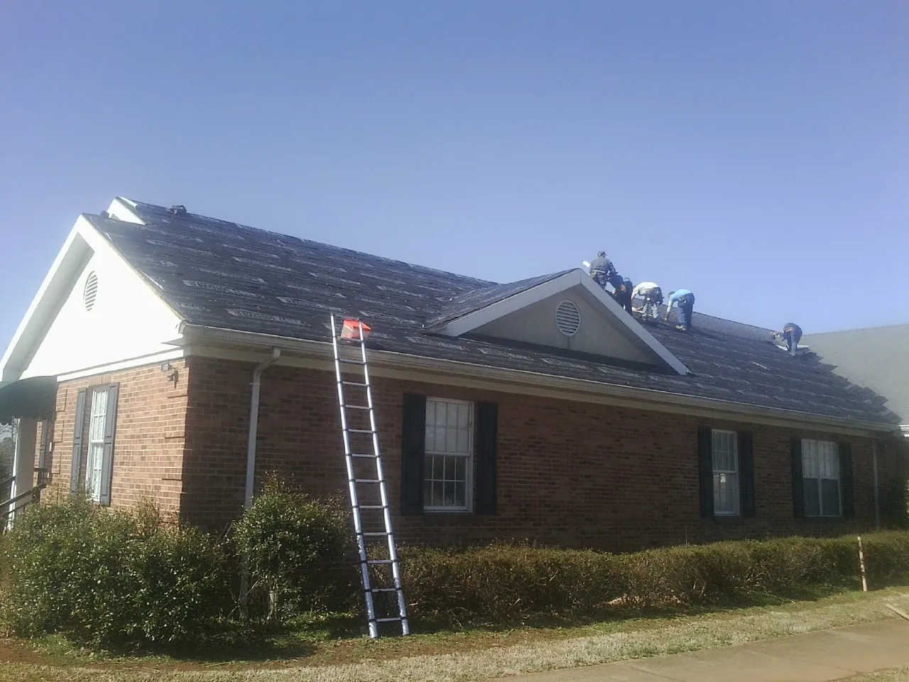 Crew tearing shingles off a brick ranch roof with a ladder set — Emergency Roof Repair work by our crew in Mount Marion