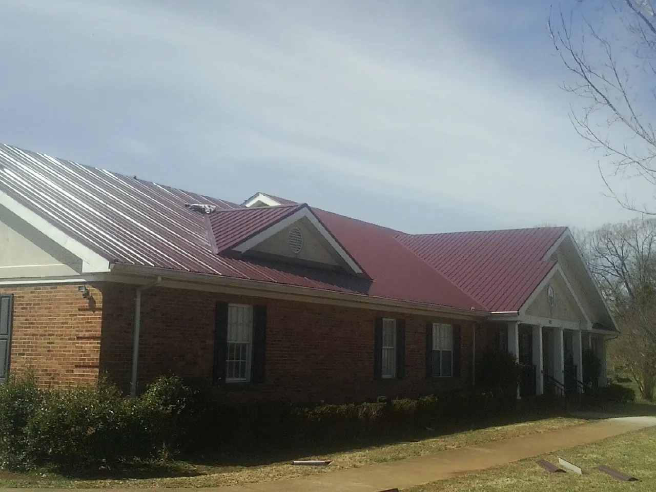 Red metal roof with gabled entries on a long brick building, from a Hail Damage Roof Repair job in Mount Marion