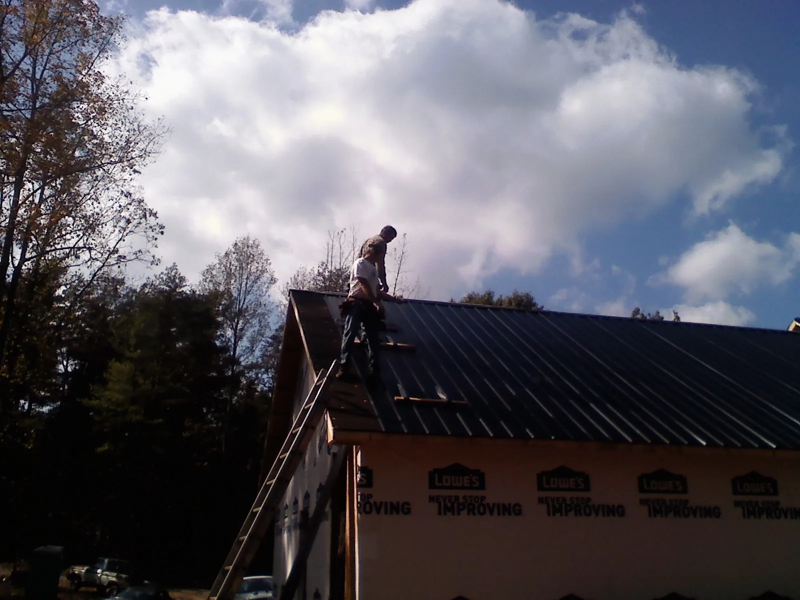 Roofer fastening dark metal panels high against a cloudy sky, from a Roof Inspection job in Mount Marion