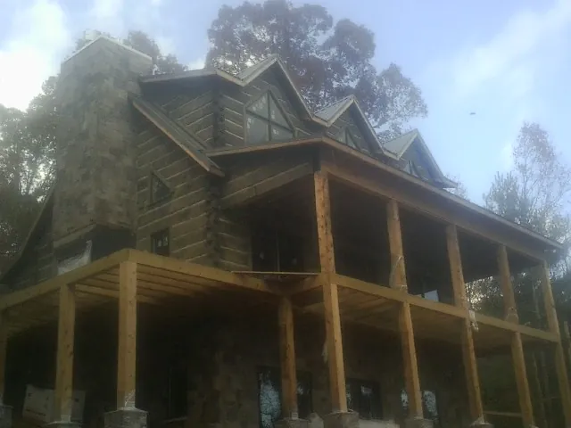 Stone chimney and dormers on a large log home with a timber porch in Mount Marion