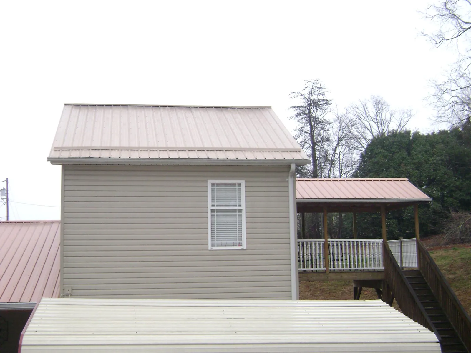 Tan metal roofs on a two story addition and attached porch, from a Roof Replacement job in Mount Marion